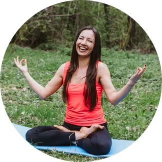A joyful woman seated outdoors in a yoga pose, performing Sri Sri Yoga Level 2