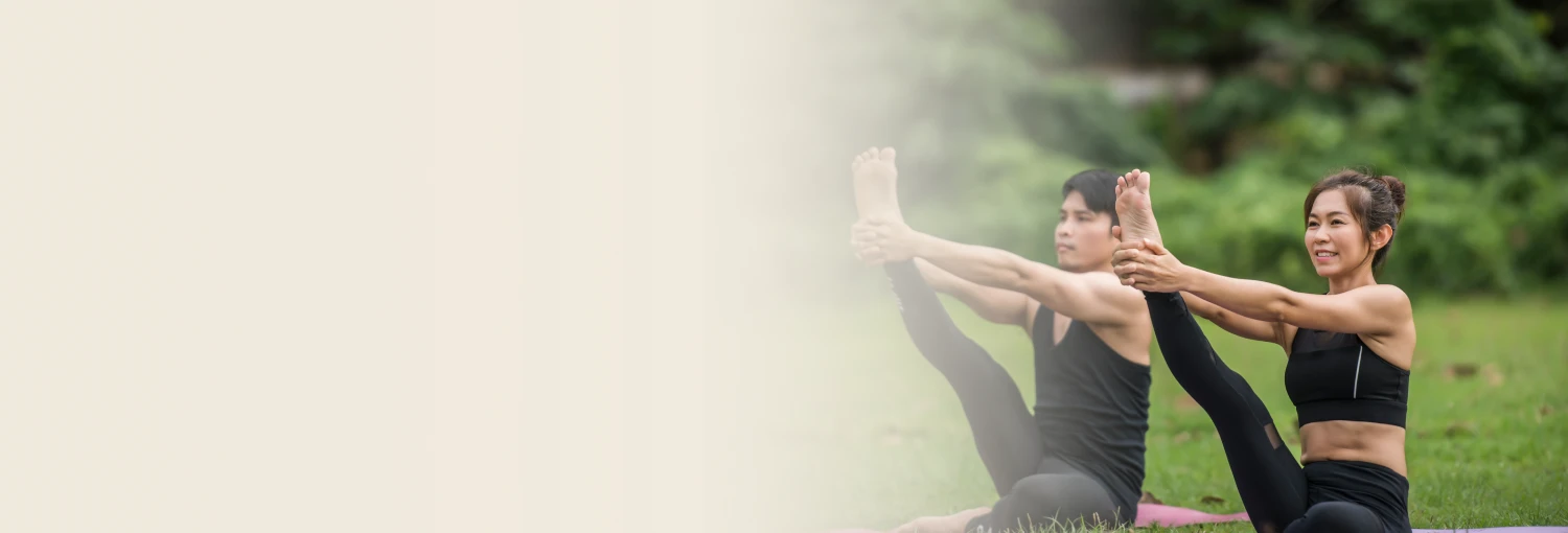 Man and woman practicing a seated leg stretch pose in a sri sri yoga session on the grass