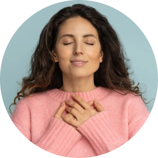 Woman in pink sweater expressing gratitude and inner peace with hands on heart