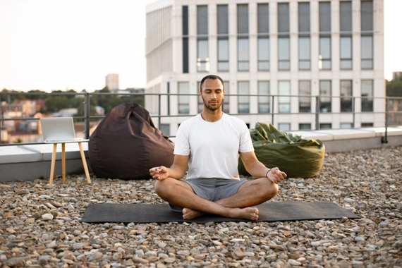 A man sitting in a open space, eyes closed, focusing on rhythmic breathing.