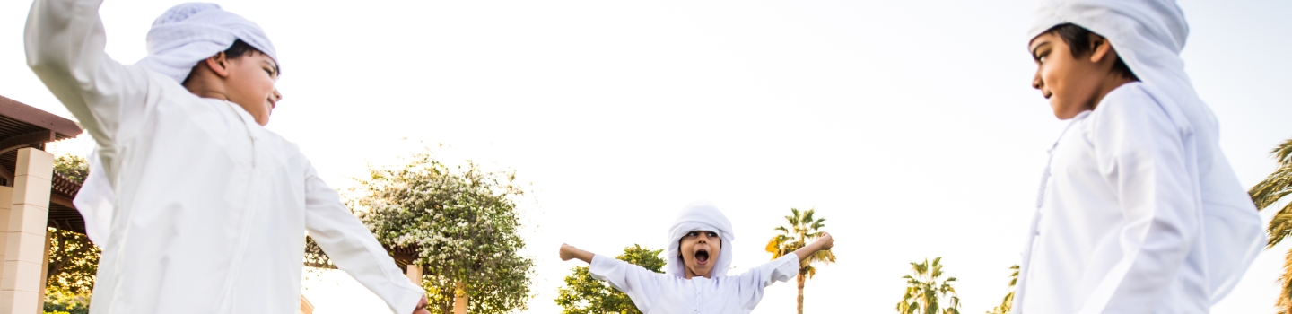 Three children in thobe playing with footlball in grass field 