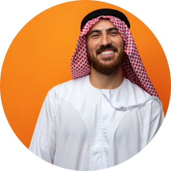 A man in Thobe standing in front of orange wall and smiling brightly