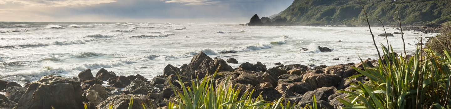 Majestic snowy mountains reflect in Lake Tekapo, framed by lush green fields under a softly lit, cloudy sky.