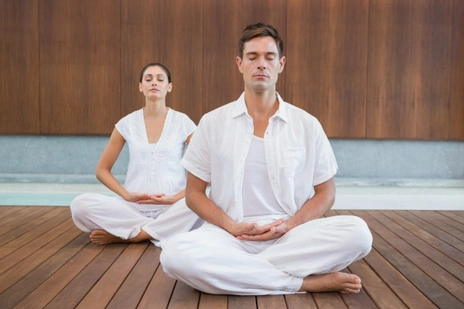 A man and a woman dressed in all white meditating in an indoor space
